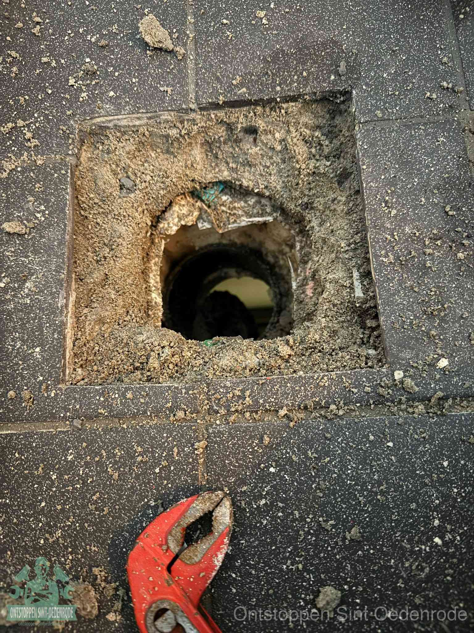 Een geopend rioolputje in een betontegelvloer met losgemaakt rooster en een zichtbare ronde afvoerbuis, het achterhalen waar de afvoerverstopping zit in Sint Oedenrode