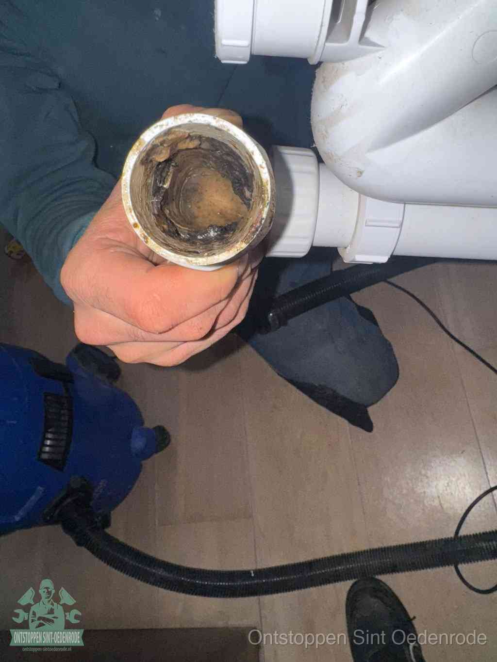 Een hand houdt een losgekoppeld PVC-afvoerbuisstuk vast dat van binnen volledig is dichtgeslibd met vet, vuil en aanslag, de meest voorkomende oorzaak van een verstopte afvoer in Sint Oedenrode