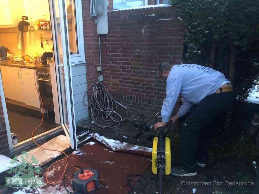 Een monteur werkt buiten bij een open riool-/grondput met een elektrische ontstoppingsmachine om een verborgen afvoerprobleem op te sporen in Sint Oedenrode