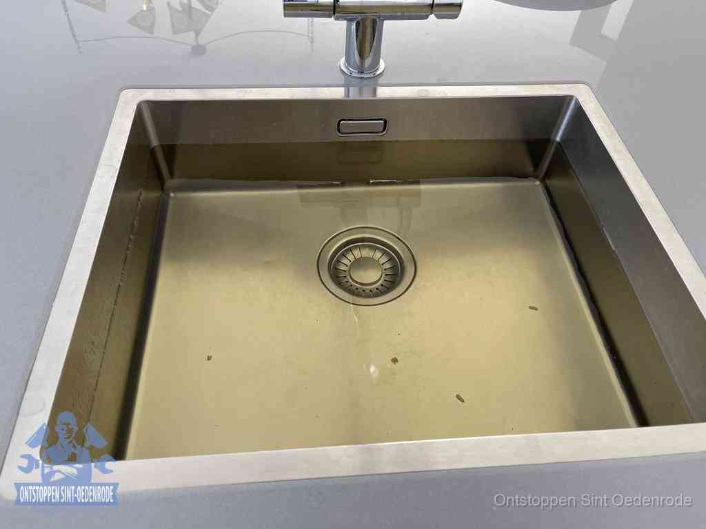 Stilstaand water in een rvs spoelbak dat niet wegloopt, een duidelijk signaal van een gootsteenverstopping in Sint Oedenrode
