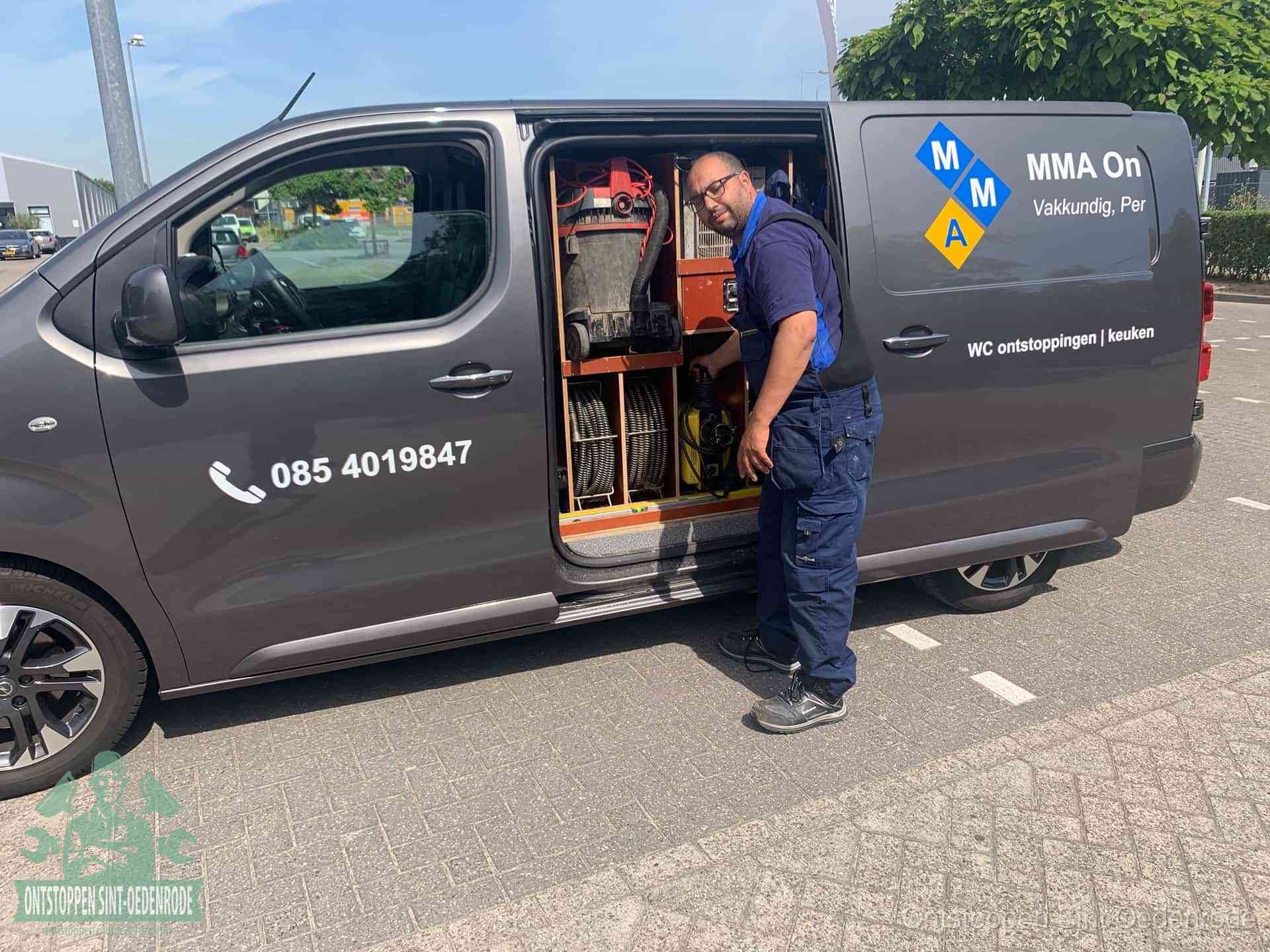 Een monteur bij de open schuifdeur van zijn bedrijfsbus op een parkeerplaats, klaar om de oorzaak van terugkerende afvoerverstoppingen aan te pakken in Sint Oedenrode