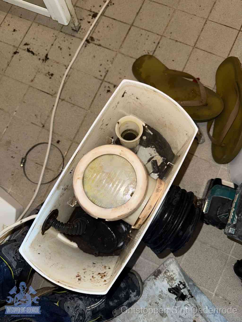 Een gedemonteerde toiletpot op de vloer met ontstoppingsveer en gereedschap ernaast, het verwijderen van een vastzittend voorwerp uit de wc in Sint Oedenrode