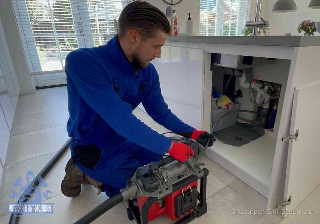 Een monteur voert een professionele elektrische ontstoppingsmachine in de afvoer onder de spoelbak tijdens het gootsteen ontstoppen in Sint Oedenrode